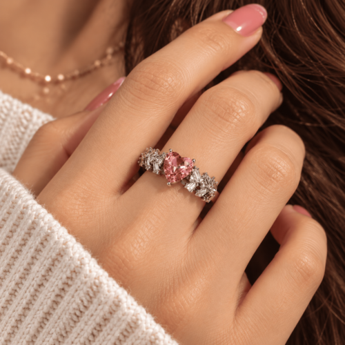 Silver-tone ring with a pink heart-shaped stone and clear side stones worn on a finger
