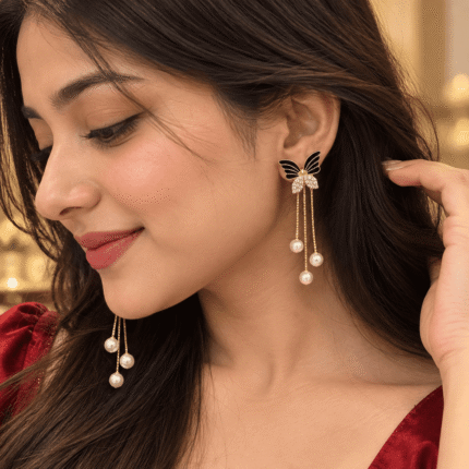 Woman wearing gold-tone butterfly earrings with black wings, clear stone details and three pearl-look chain drops