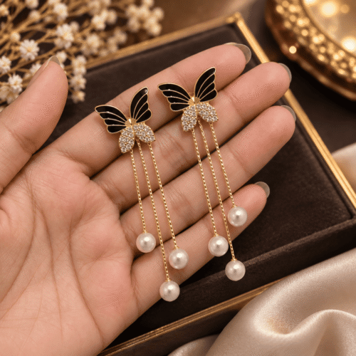 Pair of Butterfly Pearl Earrings with black wings and pearl-look chain drops held in an open palm