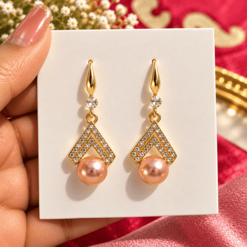 Chevron Pearl Earrings with double V-shaped clear stone details and peach pearl-look drops on a card held in a hand