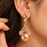 Woman wearing a gold-tone double chevron drop earring with clear stones and a peach pearl-look drop