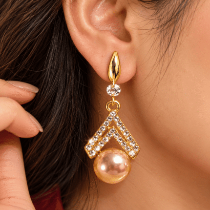 Woman wearing a gold-tone double chevron drop earring with clear stones and a peach pearl-look drop