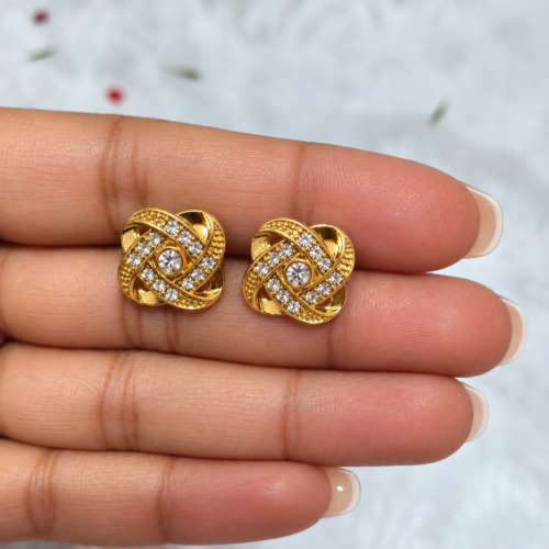 Close-up of gold-tone knot stud earrings held on fingers