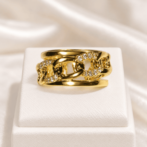 Close-up of a gold-tone chain-link ring with clear stones on a cream stand