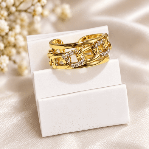 Gold-tone chain-link ring with clear stones on a white display stand