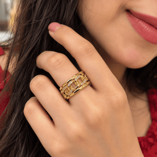 Woman wearing a gold-tone ring with chain-link details and clear stones