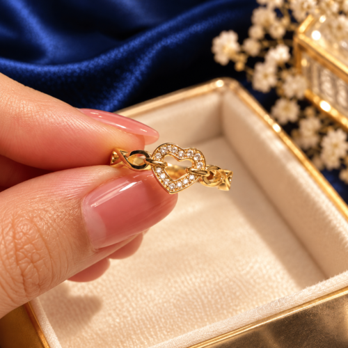 Gold-tone open-heart ring with clear stones and infinity links held between manicured fingers