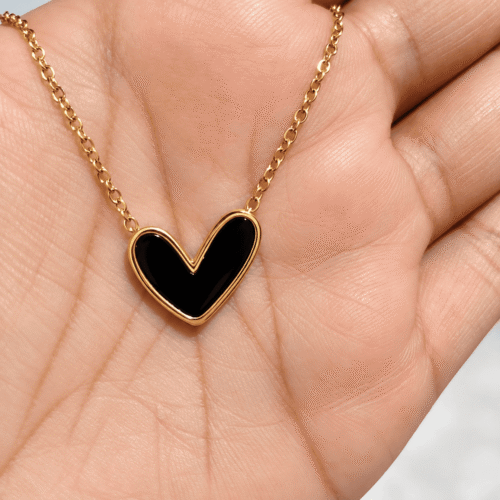 Close-up of a black heart pendant with a gold-tone border resting on an open palm