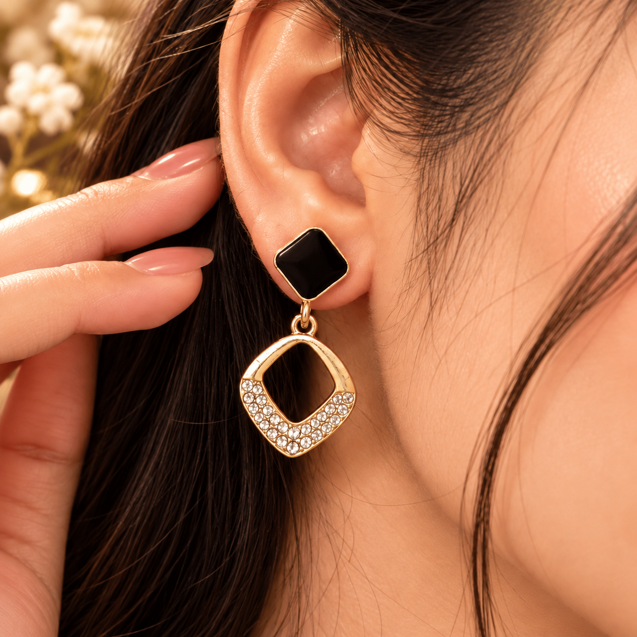 Midnight Square Earrings Worn by Woman Woman wearing a gold-tone drop earring with a black square top and open square drop with clear stone details