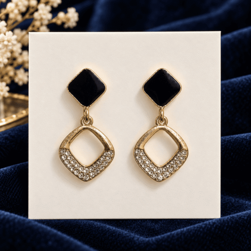 Black and gold-tone geometric drop earrings with clear stone details on a card against navy velvet