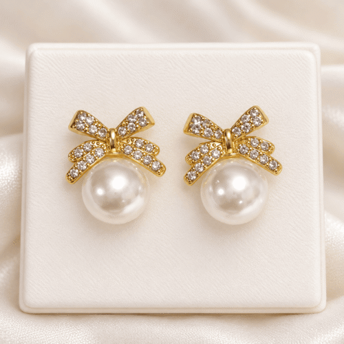Gold-tone bow earrings with clear stones and white pearl-style beads displayed as a pair