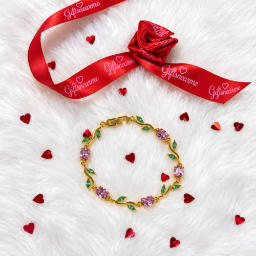 Gold-tone bracelet with pink oval stones and green leaf details on a white background