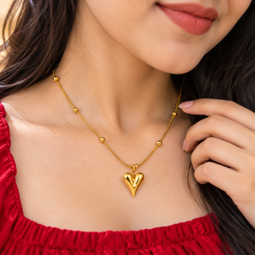 Woman wearing a gold-tone heart pendant necklace with round bead details