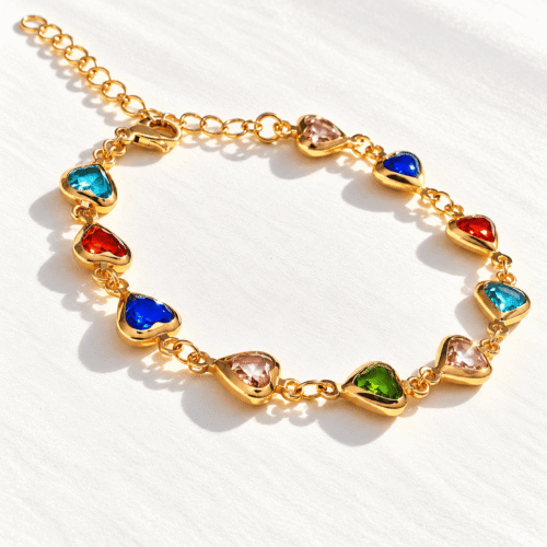 Close-up of multicolour heart-shaped stones and gold-tone links of Rainbow Heart Bracelet on a cream background