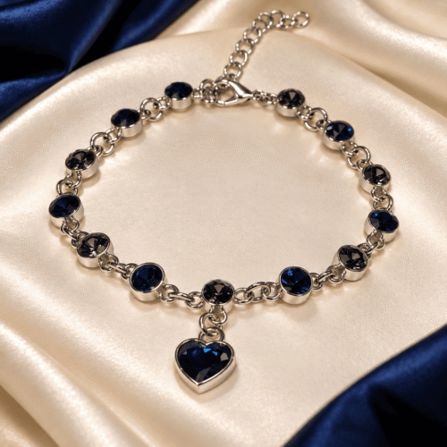Full view of Sapphire Heart Bracelet with navy-blue and smoky-grey round stones and a heart charm on ivory satin