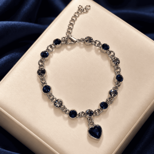 Silver-tone Sapphire Heart Bracelet with navy-blue stones and a dangling heart charm on an ivory cushion