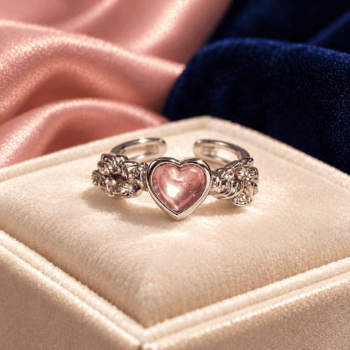 Pink heart ring with a silver-tone ornate floral band displayed on ivory velvet