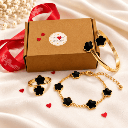 Black clover ring, cuff bangle and chain bracelet in a gold-tone finish arranged beside a gift box